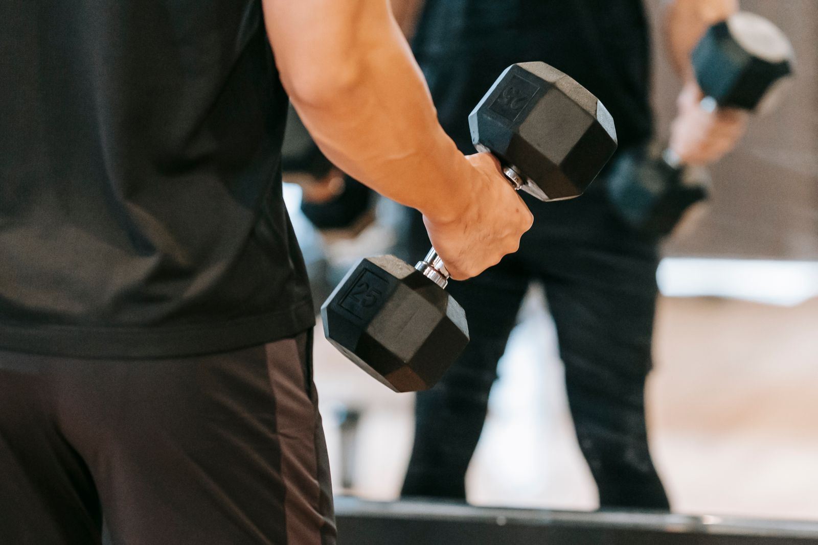Person hält eine schwarze 25-Kilo-Kurzhantel beim Bizeps-Curl im Fitnessstudio
