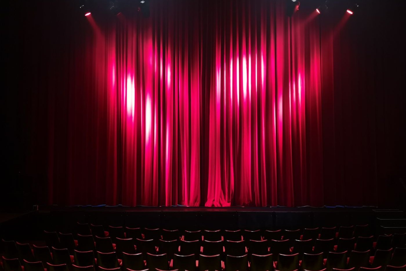 Roter Bühnenvorhang im Scheinwerferlicht vor leeren Sitzreihen eines Theaters