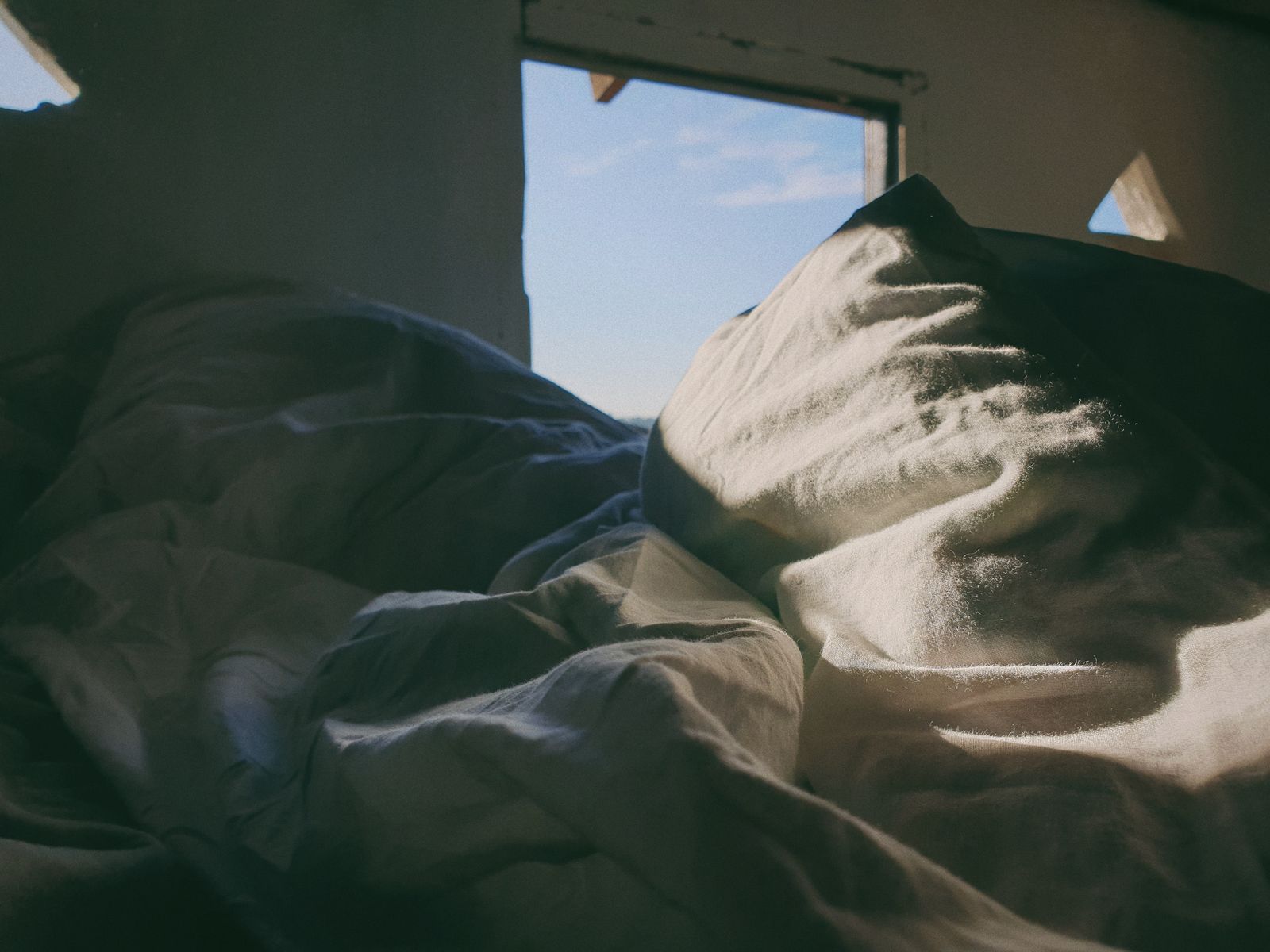 Zerknittertes leeres Bett mit heller Decke im Vormittagslicht eines Schlafzimmers
