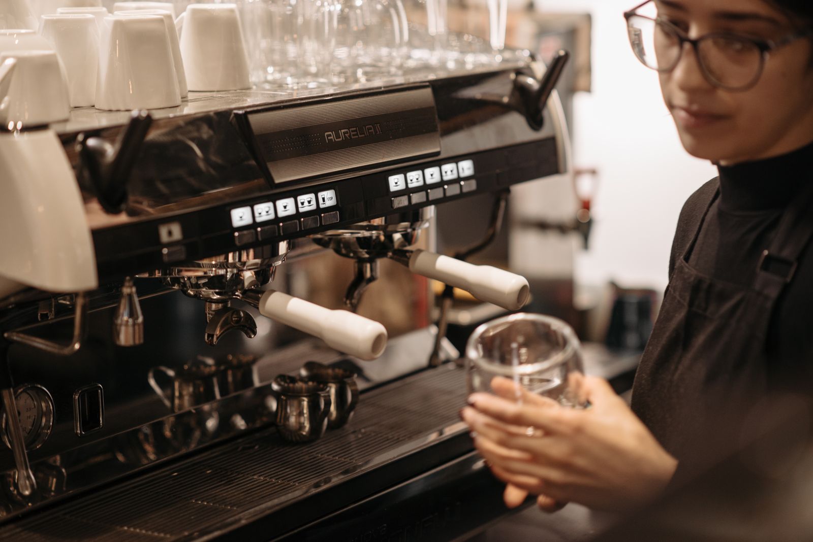 Barista mit schwarzer Schürze arbeitet an einer Espressomaschine im Café