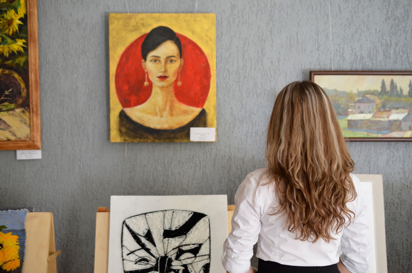 Frau steht vor einer Galeriewand und betrachtet aufgehängte Gemälde