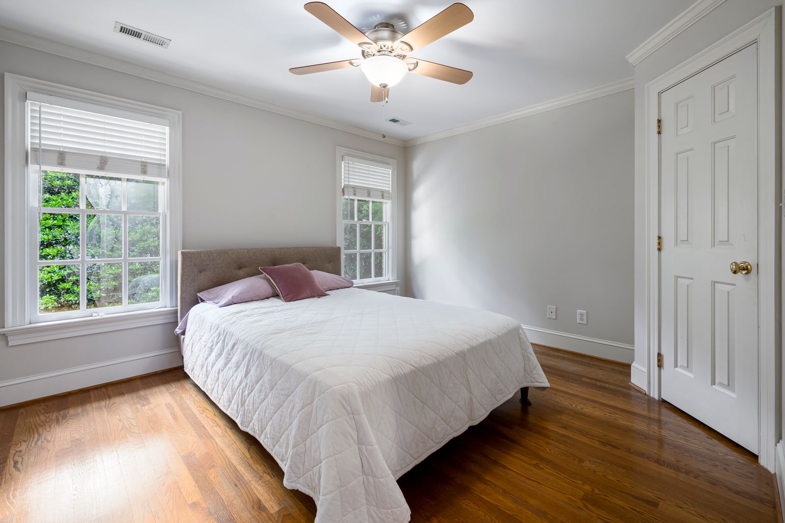 Helles Schlafzimmer mit weißer Bettwäsche, Deckenventilator und großen Fenstern