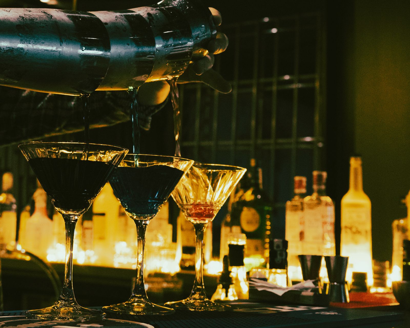 Barkeeper gießt Cocktails hinter einem beleuchteten Tresen in einer Bar