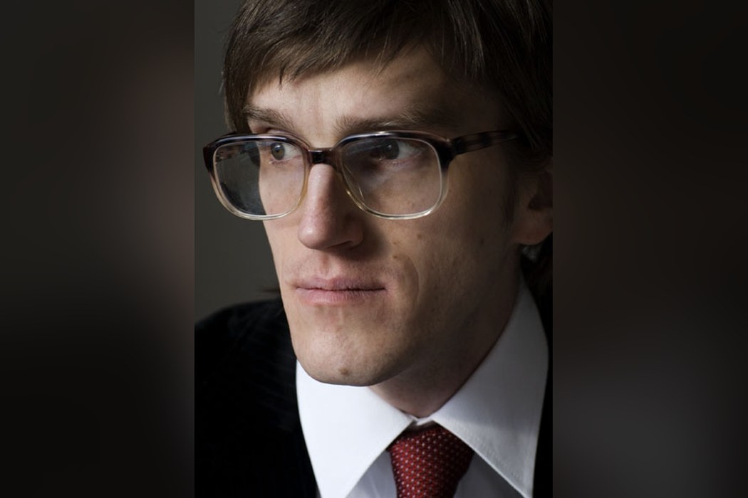 Daniel Steiner im Porträt mit Brille, weißem Hemd und roter Krawatte vor dunklem Hintergrund