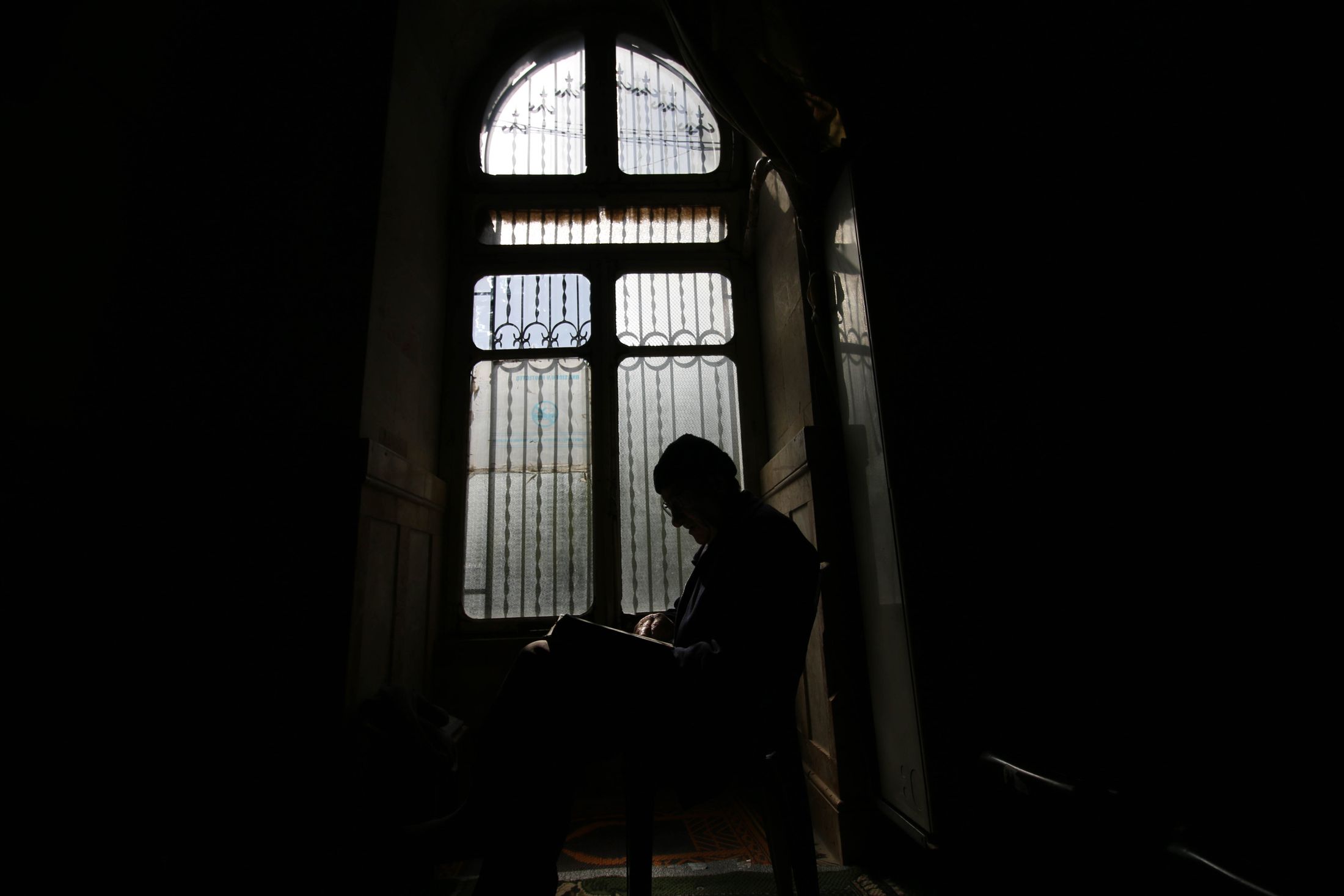 Silhouette eines Mannes, der allein am Fenster eines dunklen Raums sitzt
