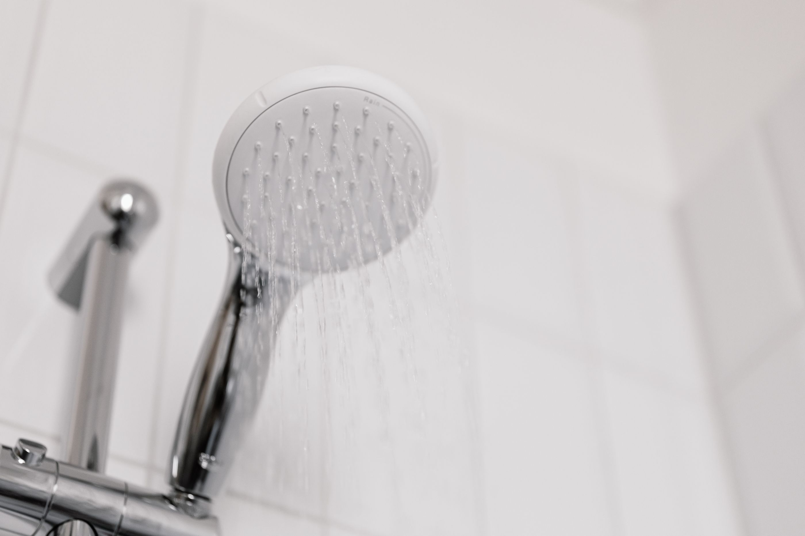 Duschkopf mit laufendem Wasserstrahl vor weißen Fliesen in einem hellen Badezimmer