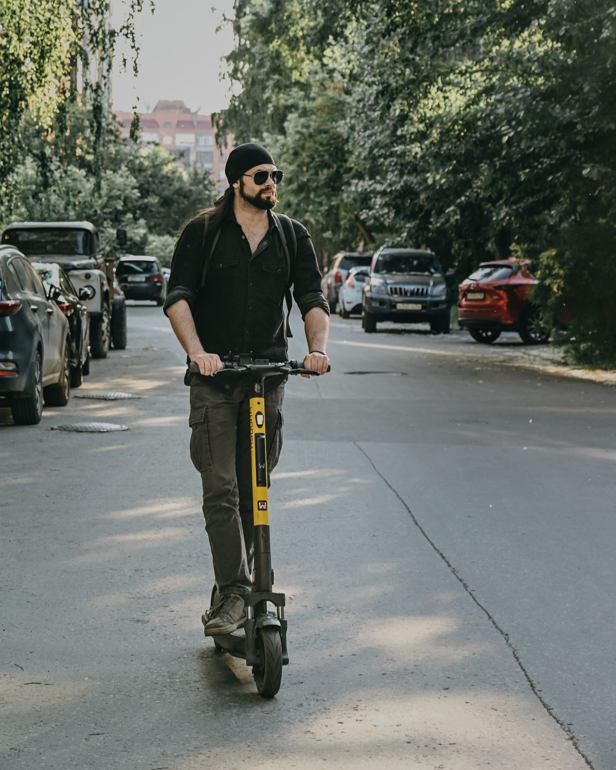 Mann fährt auf einem E-Scooter über eine von Bäumen gesäumte Straße