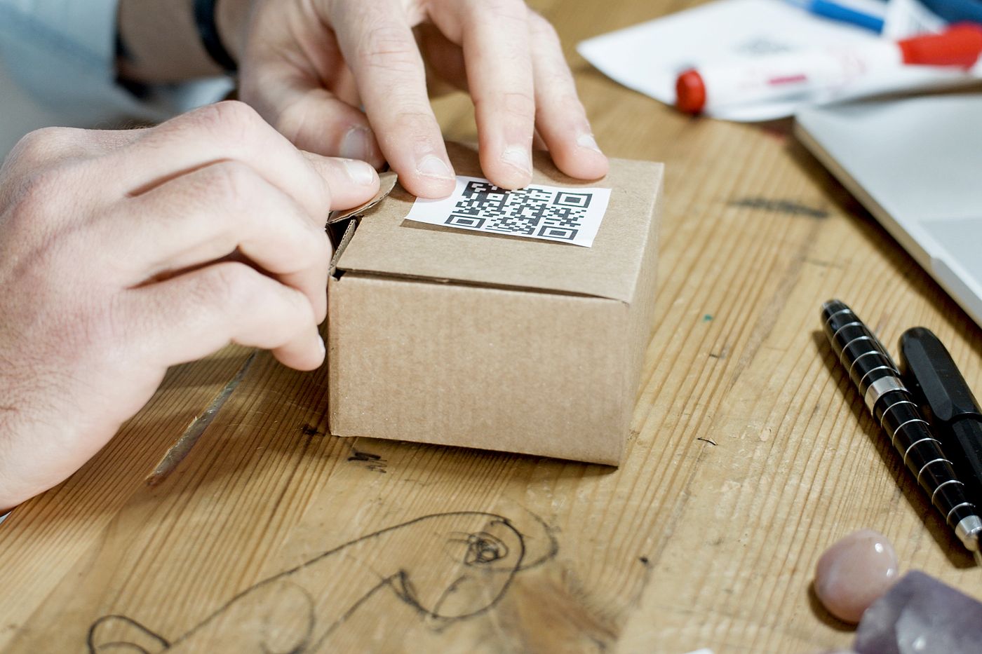 Hände halten einen braunen Versandkarton mit QR-Code-Etikett für den Versand