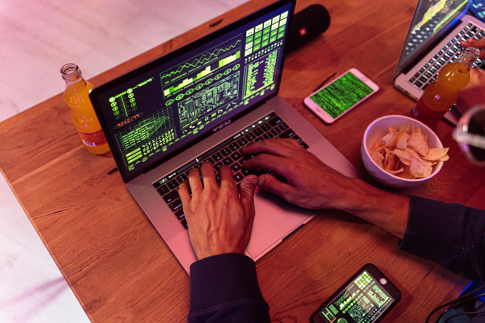 Hände tippen auf einem Laptop mit Programmcode, daneben ein Smartphone