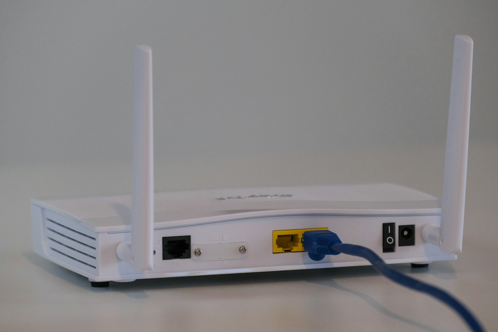 Weißer Router mit zwei Antennen, an dessen Rückseite ein blaues Netzwerkkabel steckt