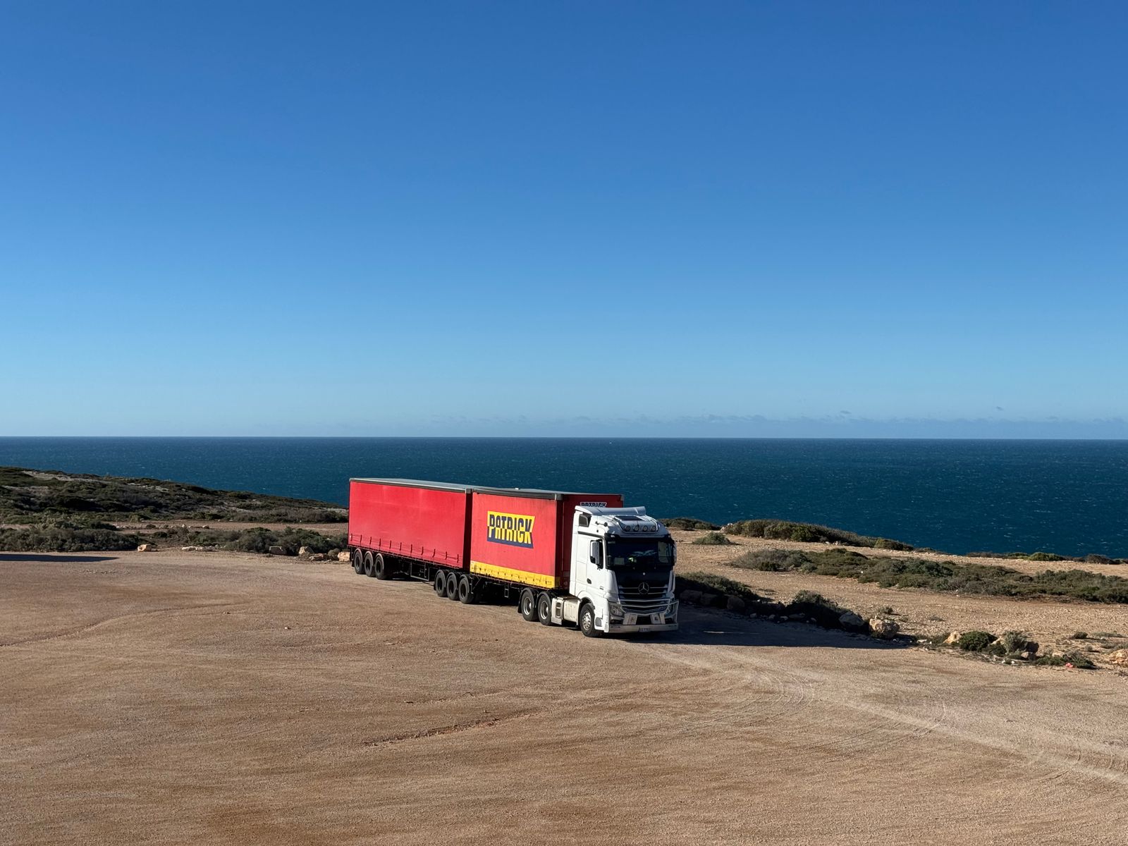 Weißer Lkw mit rotem Anhänger auf einer Küstenstraße am Meer