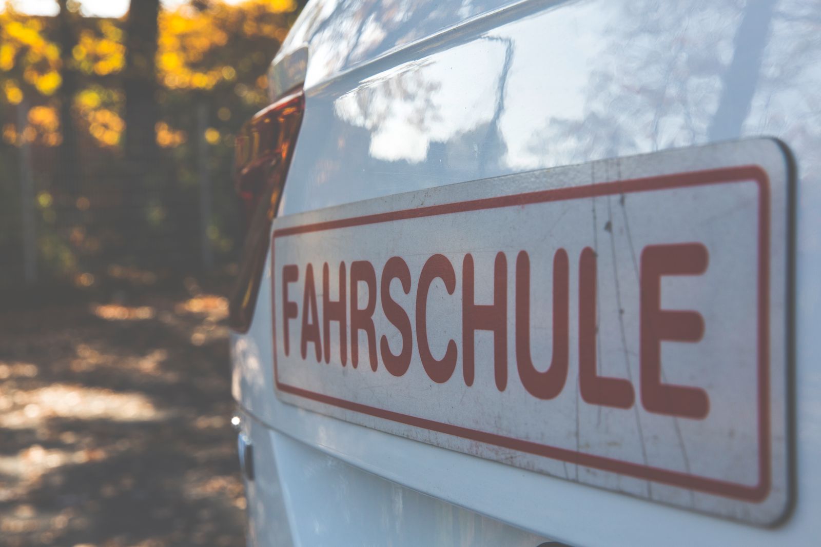 Fahrschulschild auf einem weißen Auto vor herbstlichen Bäumen