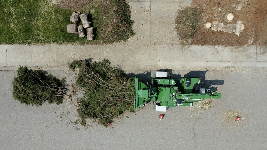 Grüner Häcksler von oben, daneben liegen aufgeschichtete Nadelbaumäste und gesägte Holzstämme