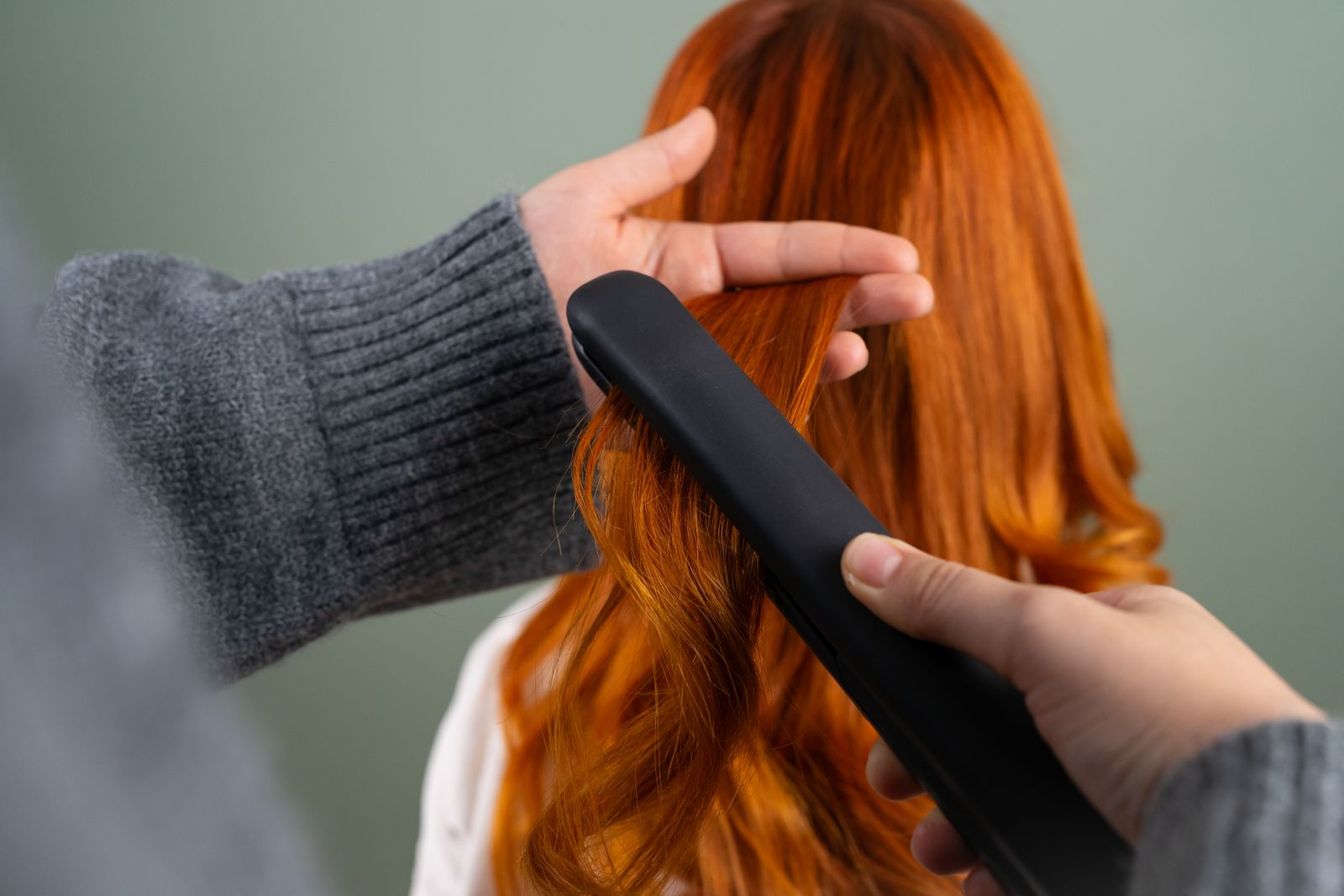 Hände glätten lange rote Haare mit einem schwarzen Glätteisen