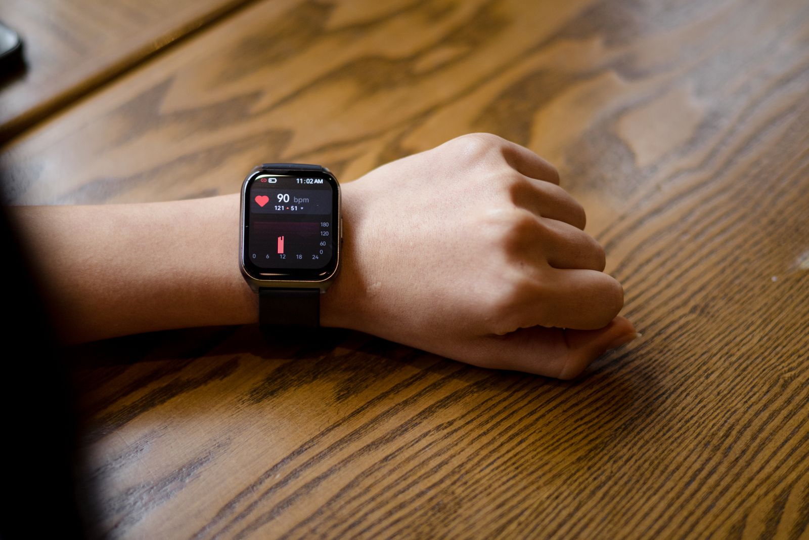 Smartwatch am Handgelenk zeigt die gemessene Herzfrequenz, der Arm liegt auf einem Holztisch