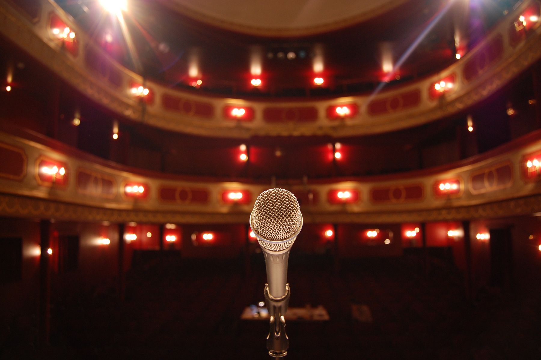 Silbernes Gesangsmikrofon auf einer Theaterbühne vor beleuchteten roten Rängen