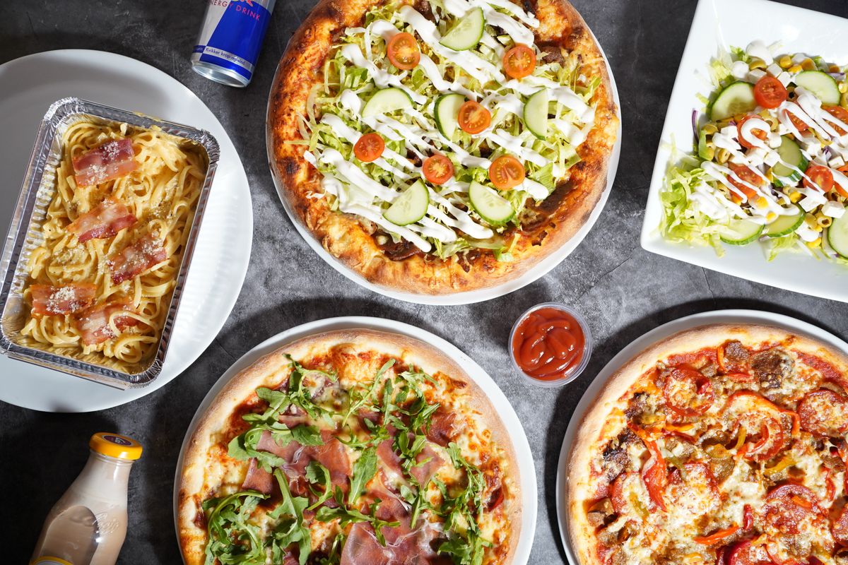 Gedeckter Tisch mit mehreren Pizzen, Pastagerichten und Salat von oben