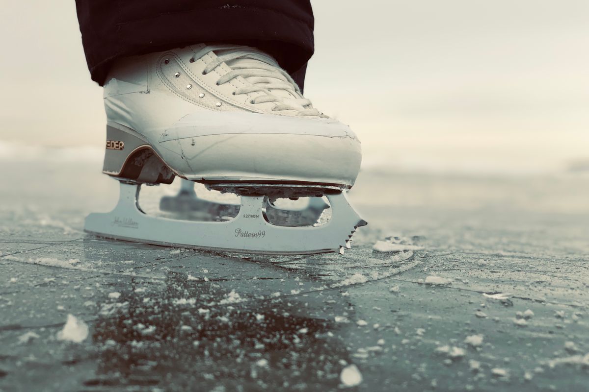 Weißer Eiskunstlaufschuh mit Kufe auf einer zerkratzten Eisfläche im Freien, Nahaufnahme