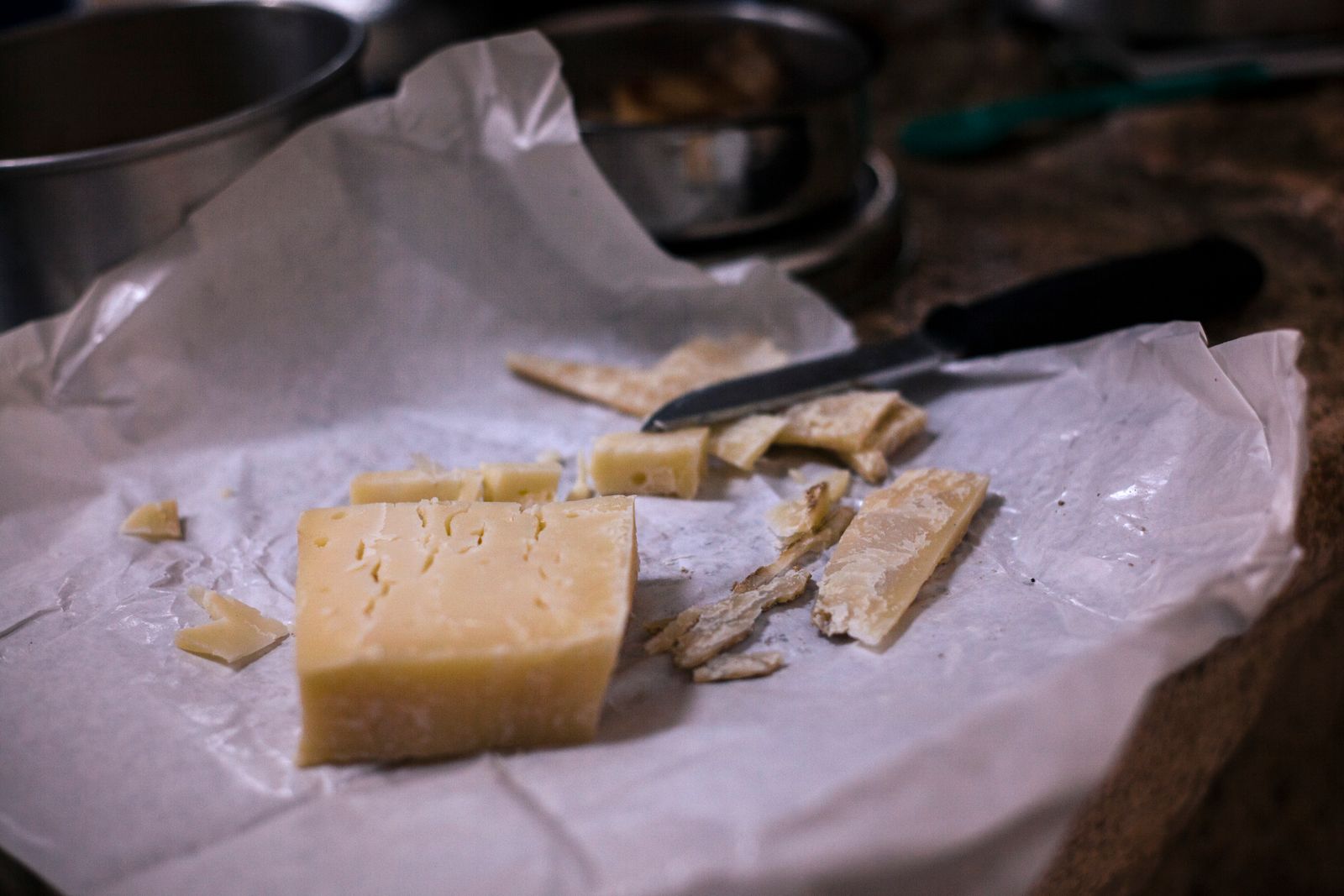 Stück Hartkäse mit abgeschnittenen Spänen und Messer auf weißem Käsepapier