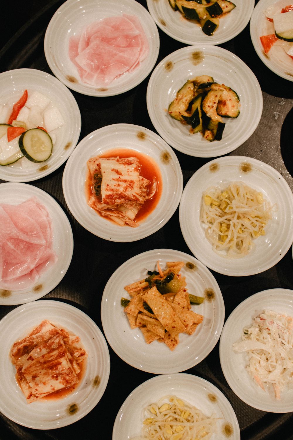 Verschiedene koreanische Banchan-Beilagen in weißen Schüsseln von oben fotografiert