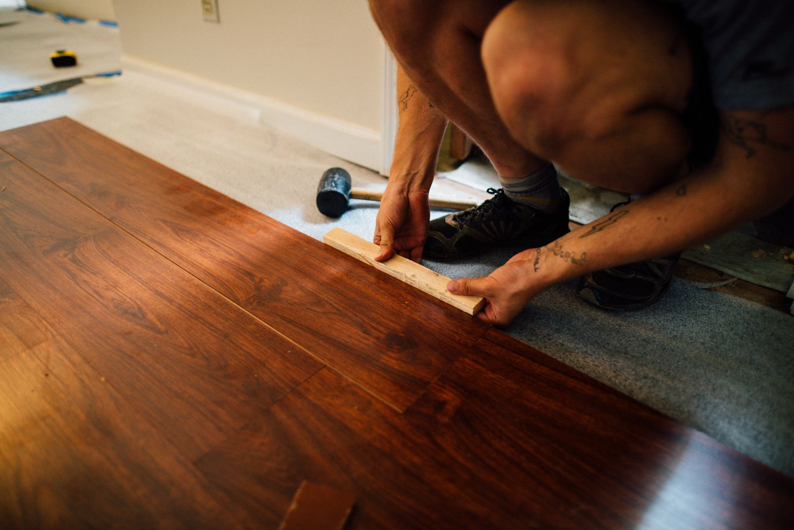 Handwerker treibt beim Verlegen ein Laminatpaneel mit einem Schlagholz in die Klickverbindung