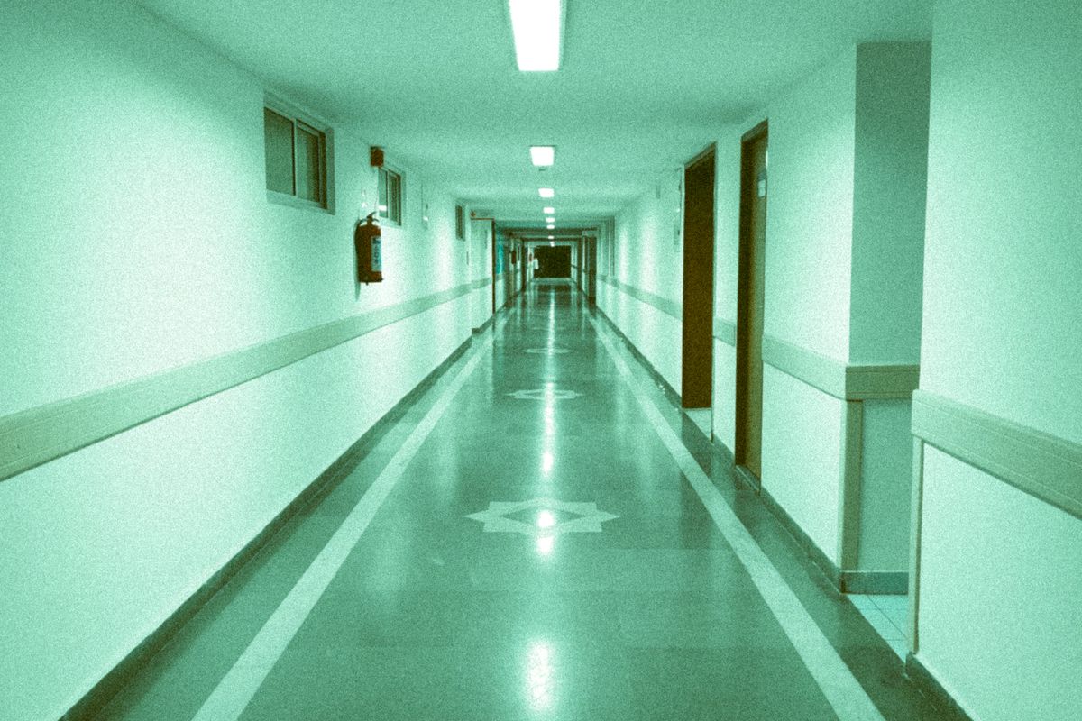 Langer, leerer Krankenhausflur mit glänzendem Boden, Türen und Deckenlampen in grünlichem Licht