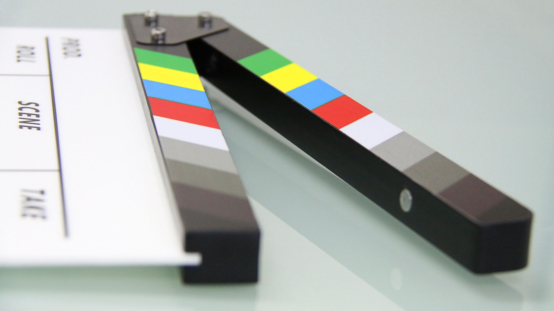 Geöffnete Filmklappe mit bunten Farbbalken liegt auf einer hellen, spiegelnden Glasfläche