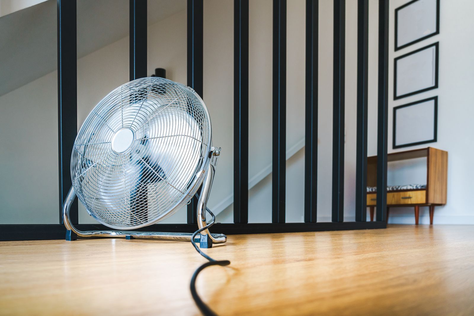 Verchromter Bodenventilator auf Holzparkett in einer hellen Wohnung vor einem Treppengeländer