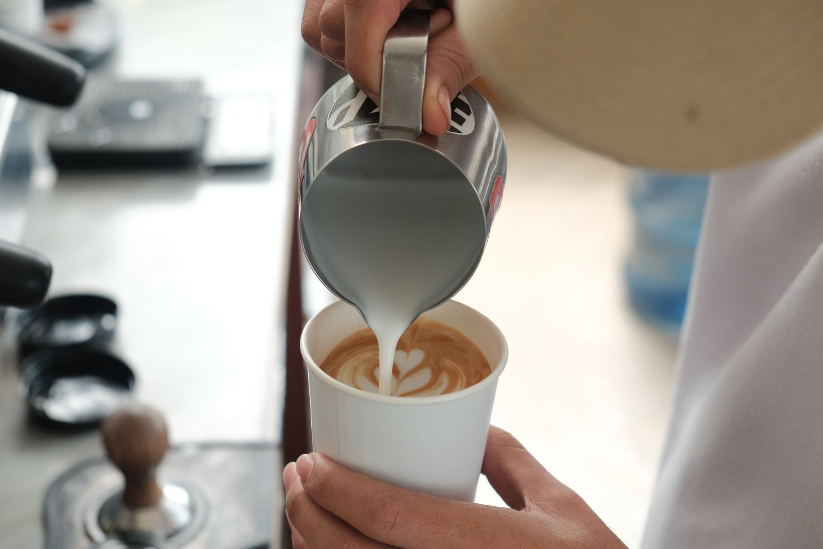 Person gießt aufgeschäumte Milch für Latte Art in eine Tasse Kaffee