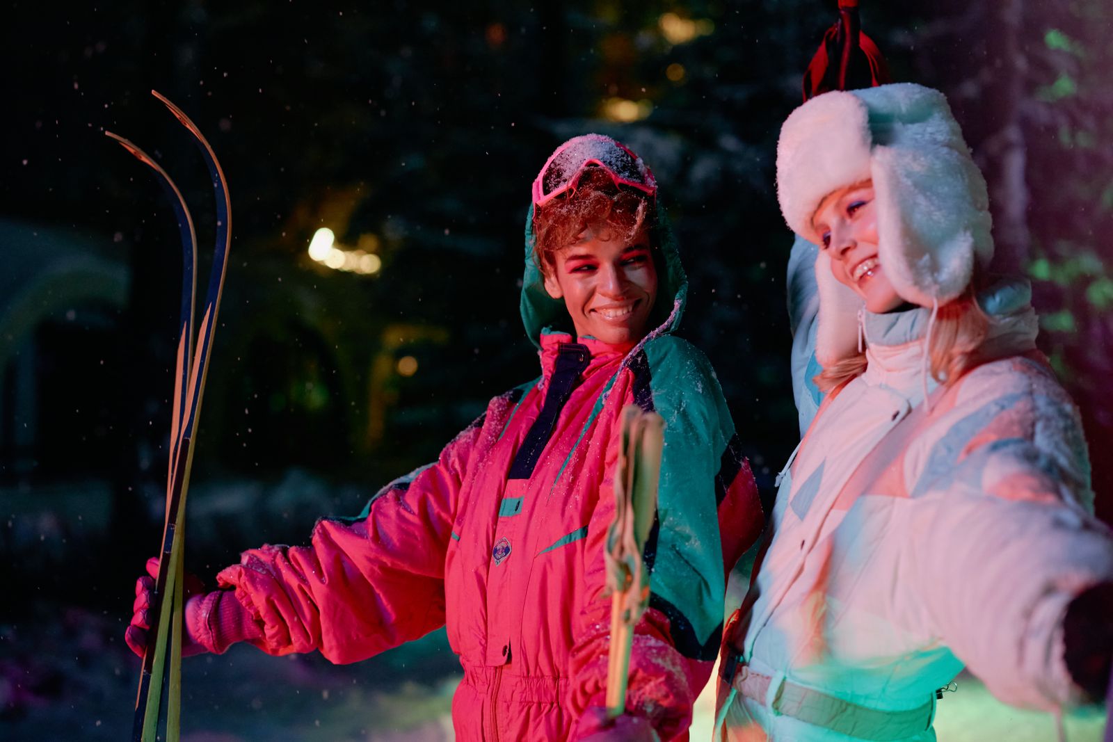 Zwei Personen in neonfarbenen Skianzügen im Schnee bei Nacht