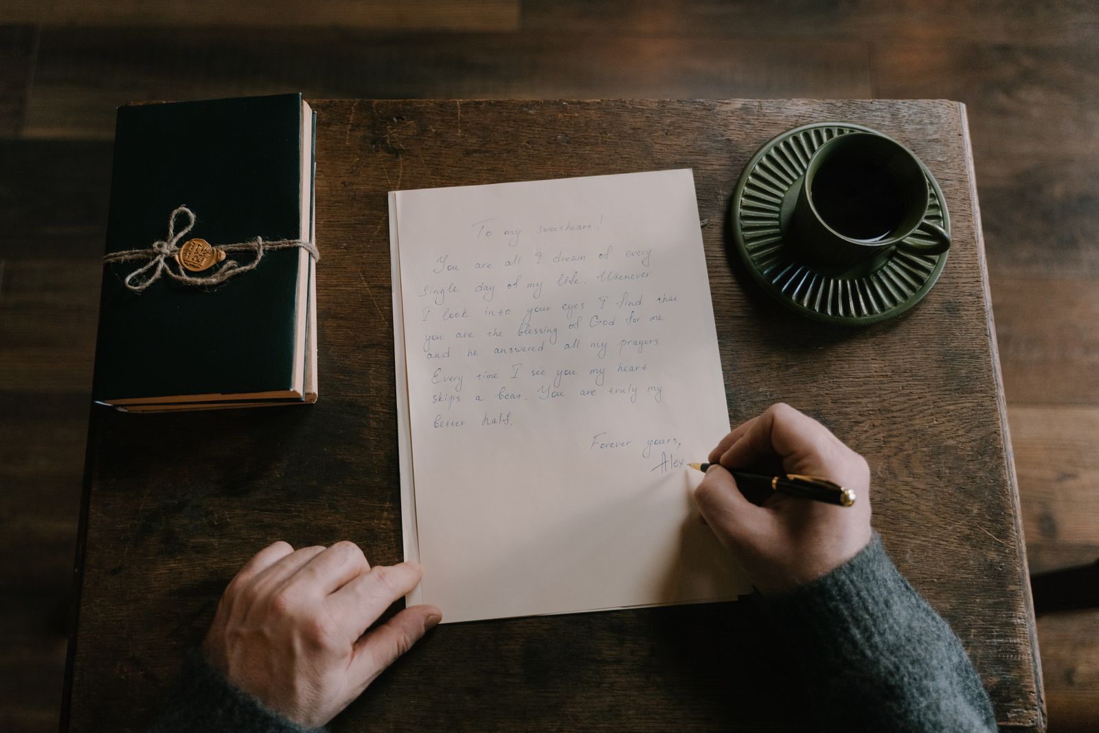 Hand schreibt mit Füller einen Brief auf einem Holztisch, daneben Kaffeetasse und Notizbuch