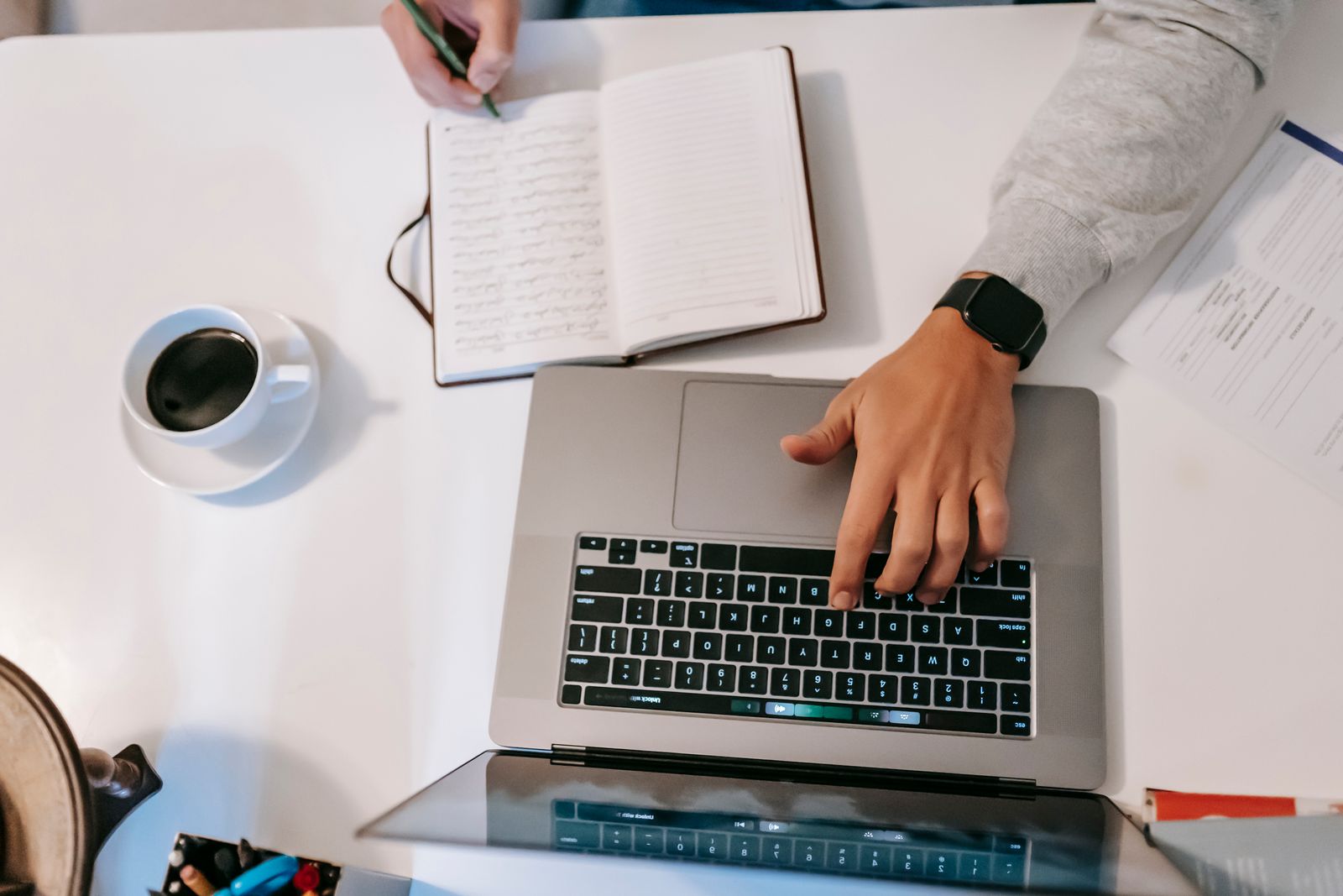 Person arbeitet abends am Laptop im Homeoffice, Notizbuch liegt daneben