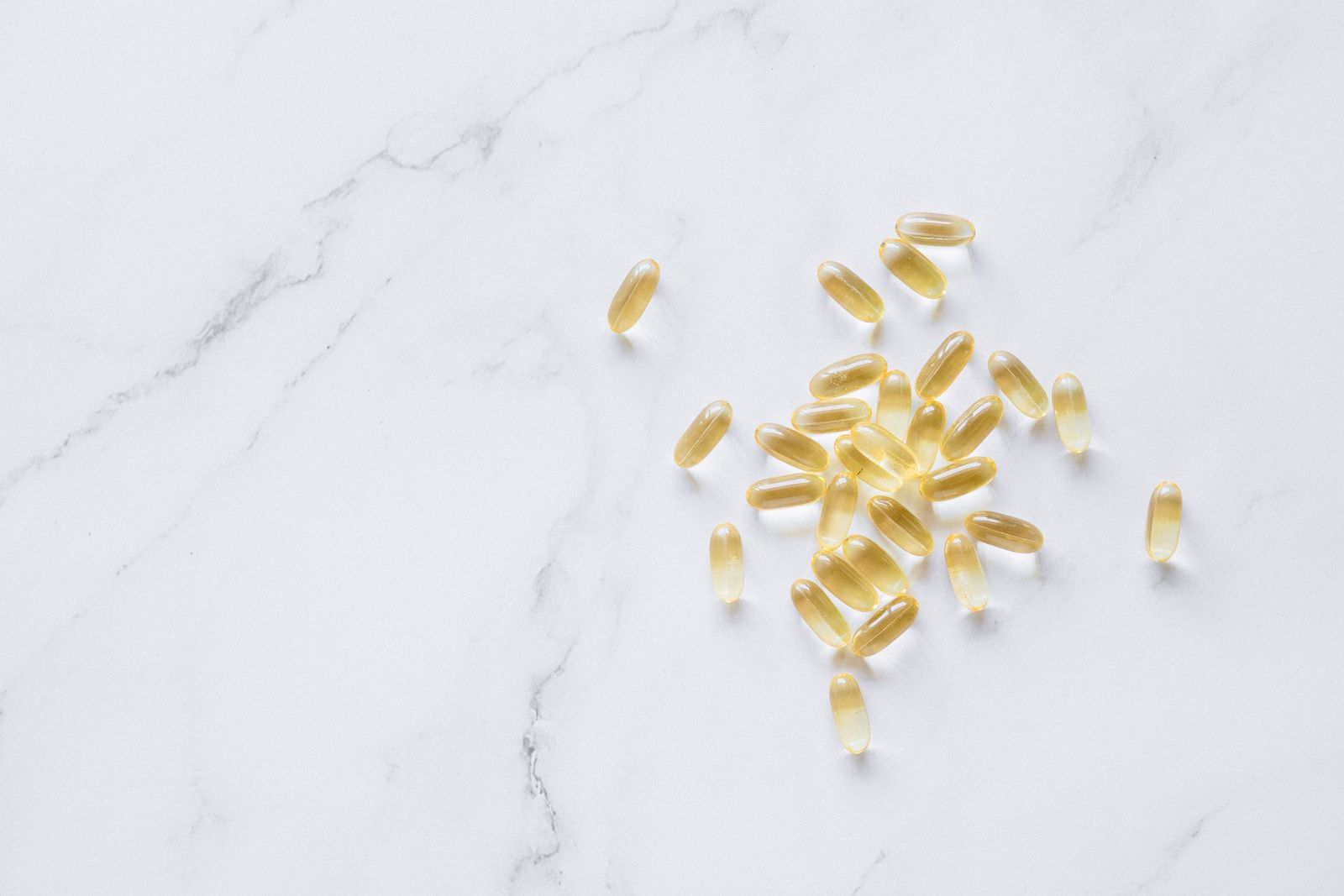 Durchsichtige gelbliche Omega-3-Fischölkapseln verstreut auf einer weißen Marmorfläche