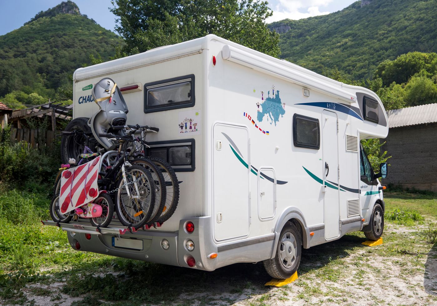 Wohnmobil mit zwei Fahrrädern auf dem Heckträger auf einer Wiese vor bewaldeten Bergen