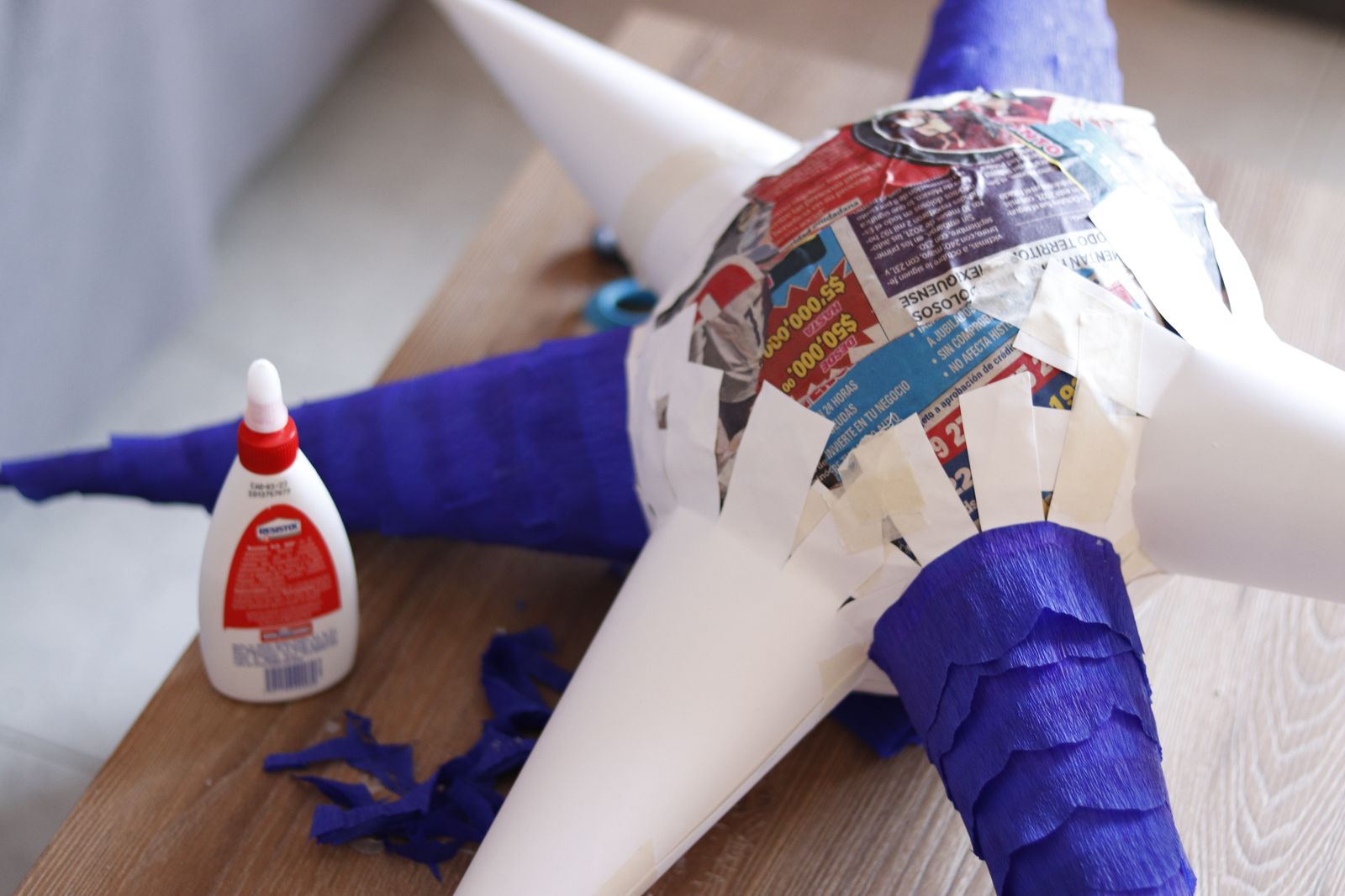 Halbfertige Piñata mit kaschierten Zeitungsstreifen und Krepppapier, daneben eine Flasche Bastelleim