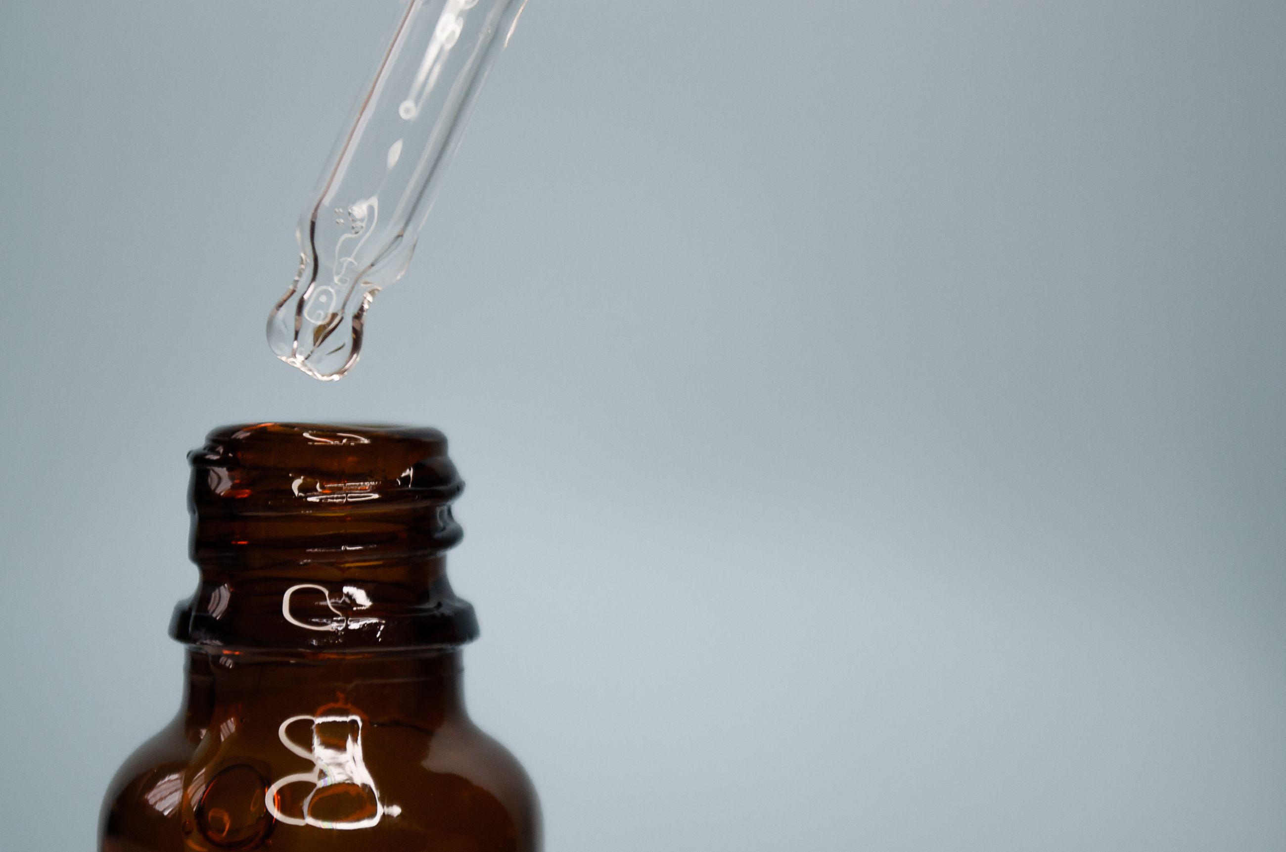 Glaspipette mit Serum über einer braunen Apothekerflasche vor neutralem Hintergrund