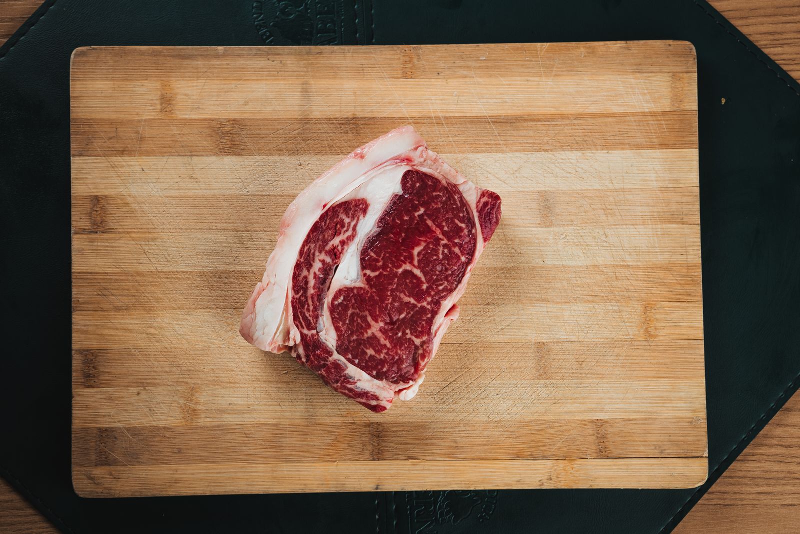 Rohes, stark marmoriertes Rib-Eye-Steak mit Fettauge auf einem Holzbrett, von oben fotografiert