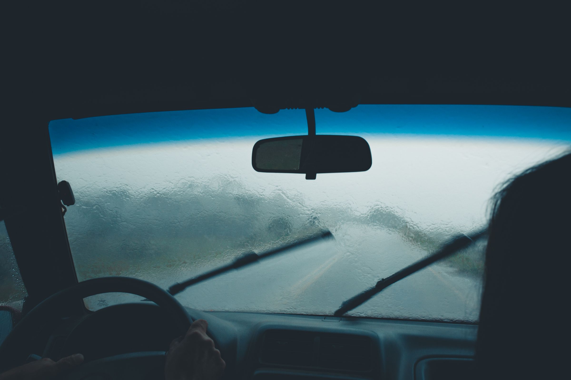 Blick aus dem Autoinnenraum auf eine regennasse Windschutzscheibe mit laufenden Scheibenwischern