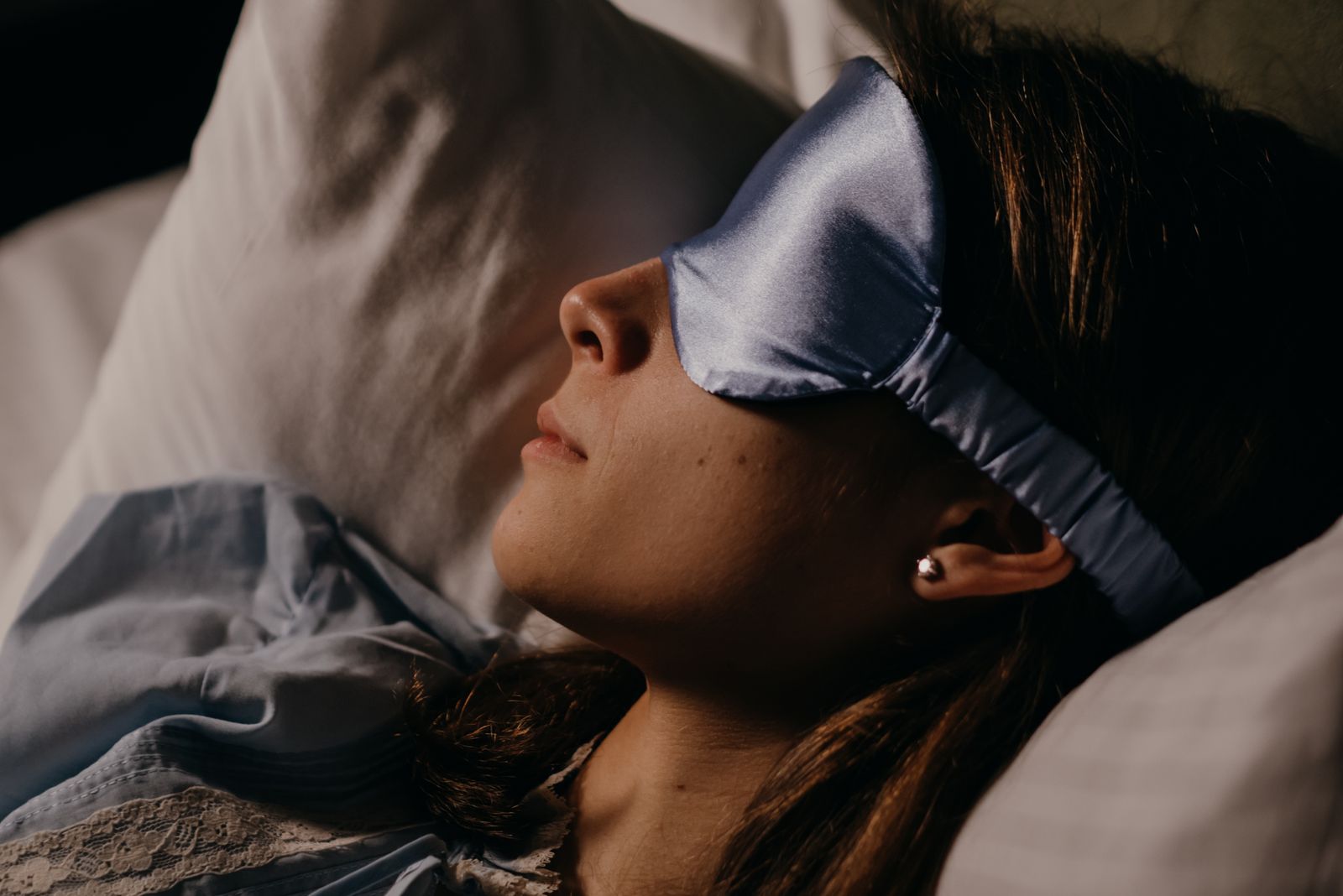 Frau schläft im Bett mit hellblauer Satin-Schlafmaske über den Augen auf einem weißen Kissen