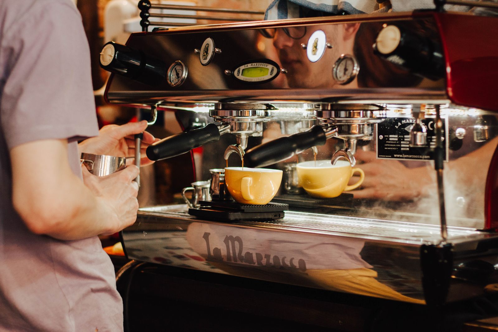 Person bedient eine Espressomaschine und zieht Espresso in eine weiße Tasse