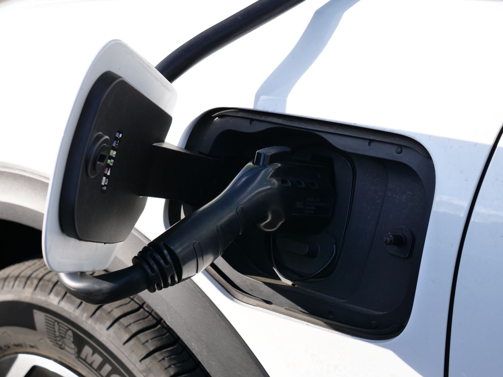 Ladestecker steckt in der Ladebuchse eines weißen Elektroautos im Sonnenlicht