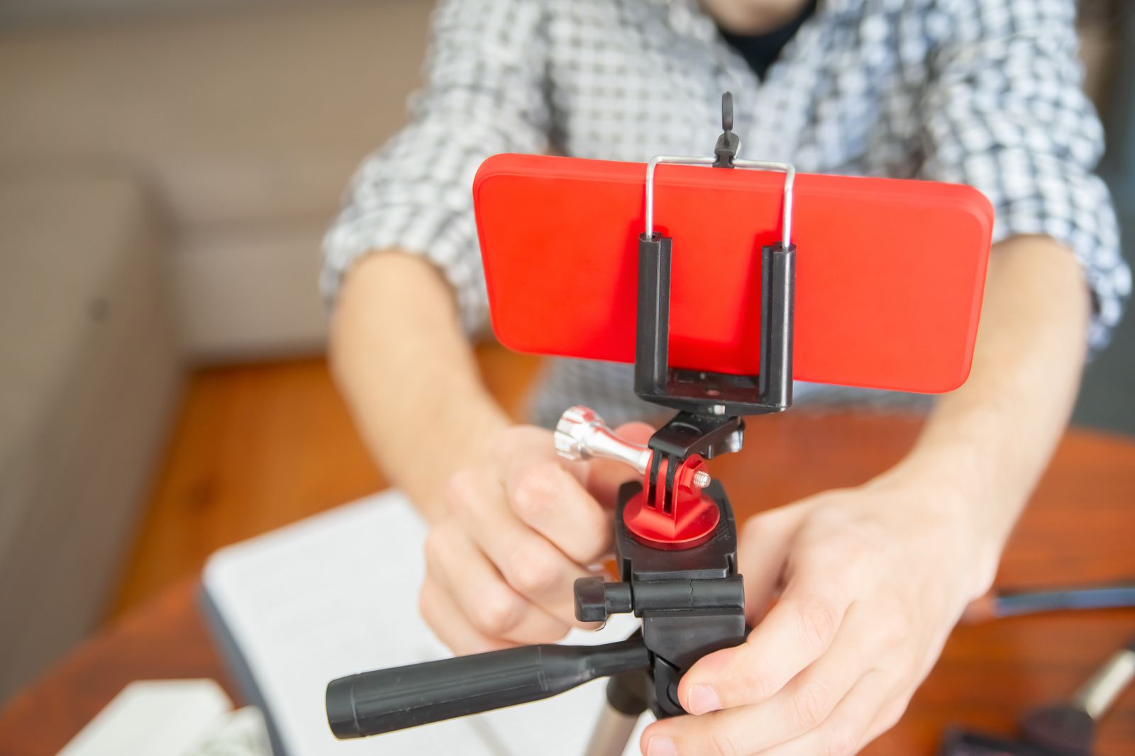 Hände richten ein Smartphone mit roter Hülle auf einem Stativ für eine Videoaufnahme aus