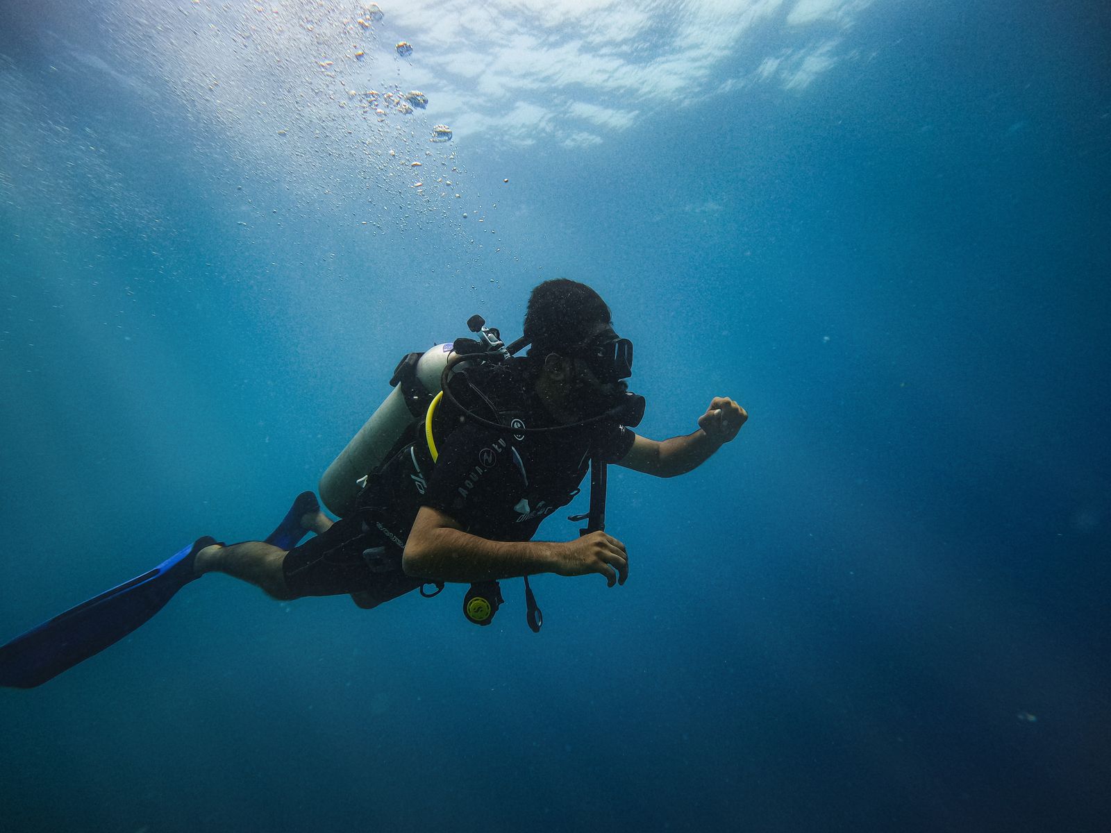Gerätetaucher in vollständiger Ausrüstung schwebt mit Flasche und Flossen im blauen Wasser