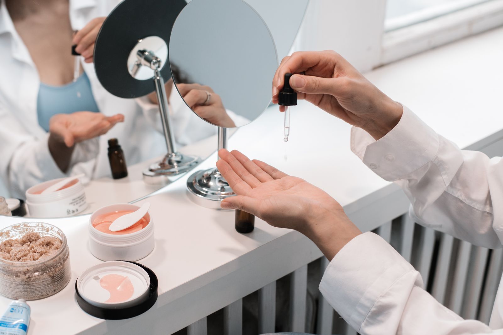 Hände tragen mit einer Pipette ein Serum auf, umgeben von Hautpflegeprodukten auf einer Ablage