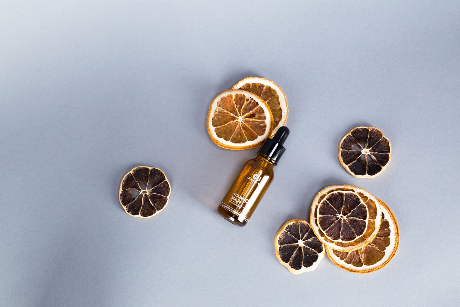 Braune Pipettenflasche mit Serum zwischen getrockneten Orangenscheiben auf grauem Untergrund