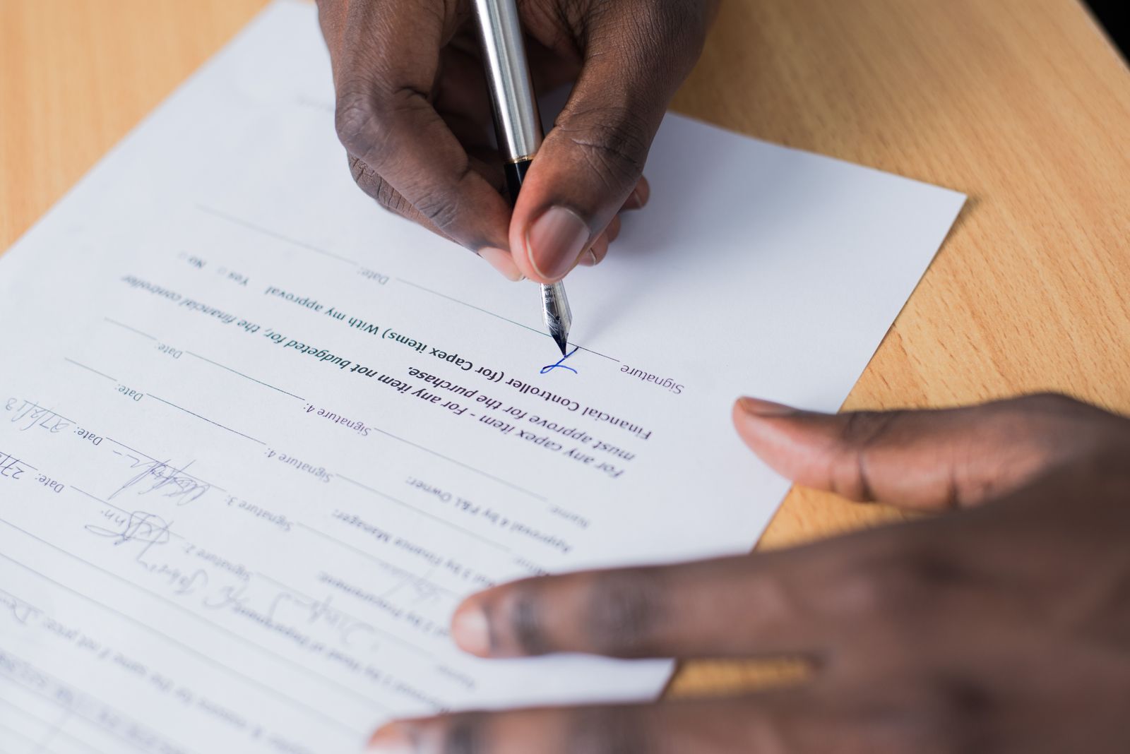Hand unterschreibt mit einem silbernen Stift ein Formular auf einem Holztisch
