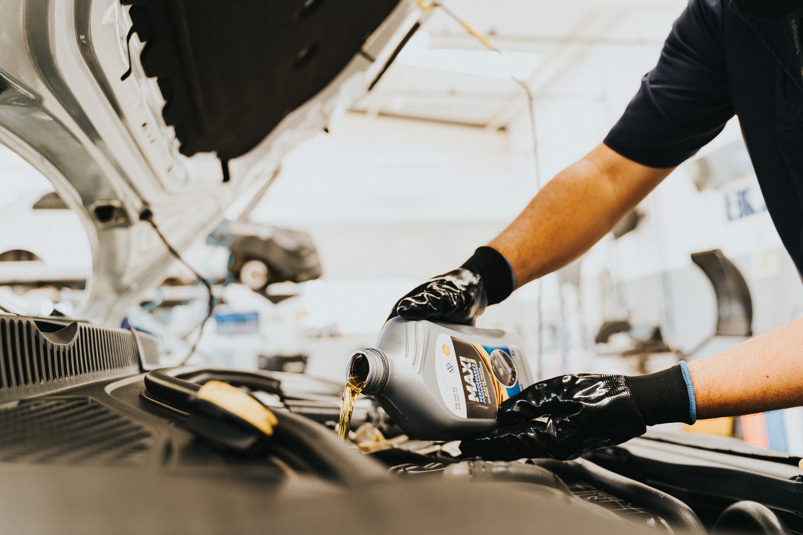 Hände in Arbeitshandschuhen füllen frisches Motoröl aus einem Kanister in einen Automotor