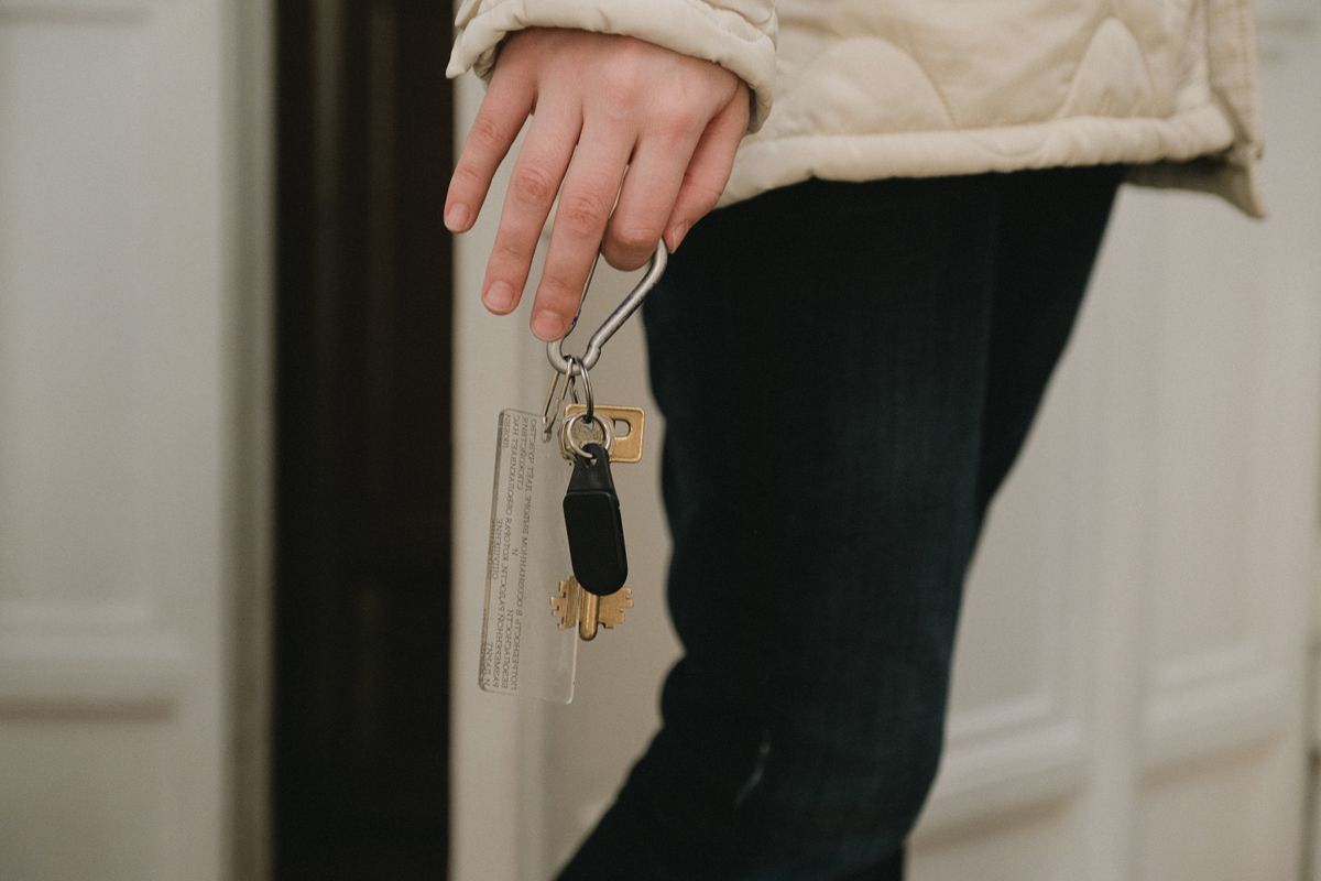 Person in heller Steppjacke hält an einer weißen Wohnungstür einen Schlüsselbund mit Anhänger