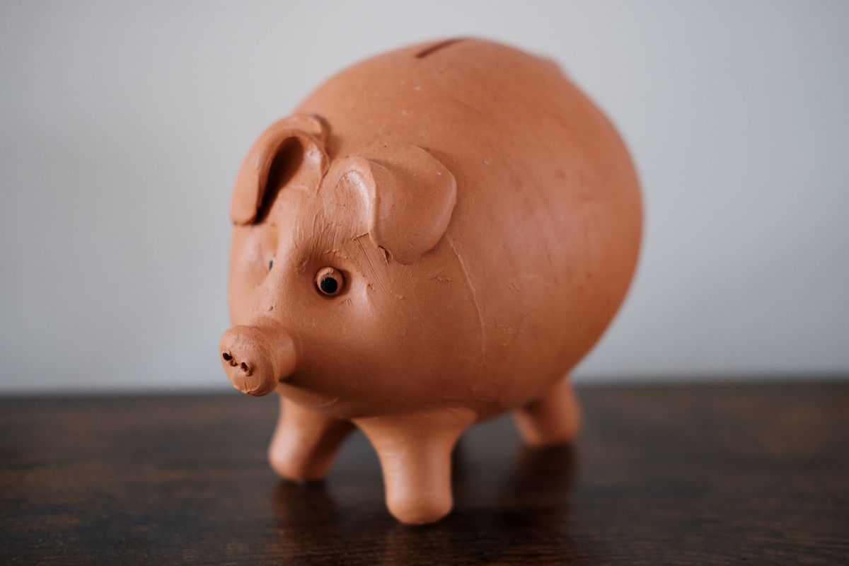 Sparschwein aus Terrakotta steht auf einem dunklen Holztisch vor einer hellen Wand