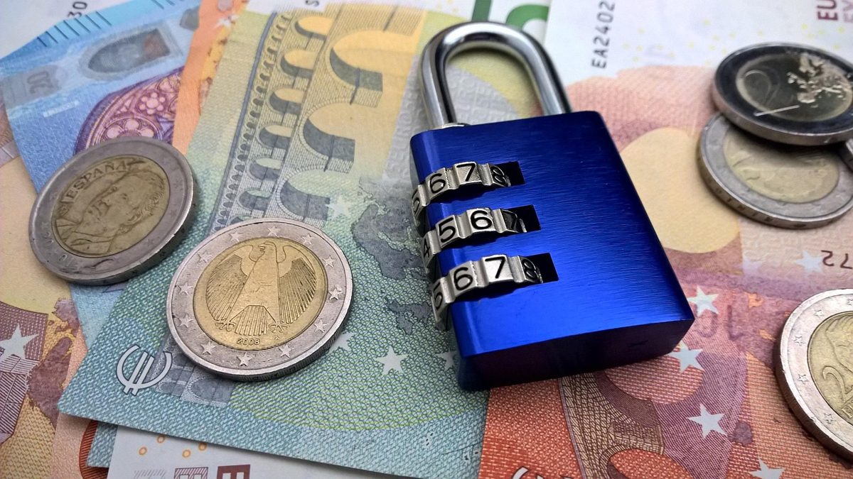 Euro-Banknoten und Münzen liegen auf einer Fläche, darauf ein blaues Zahlenschloss